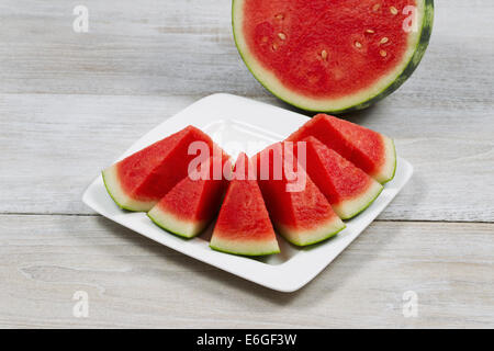 Libre de droit de tranches de melon d'eau douce sur plaque blanche avec demi-melon en arrière-plan Banque D'Images