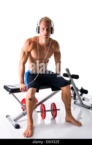 Portrait d'un jeune homme blond musclé soulevant des poids et d'écouter de la musique dans les écouteurs, isolé sur fond blanc Banque D'Images