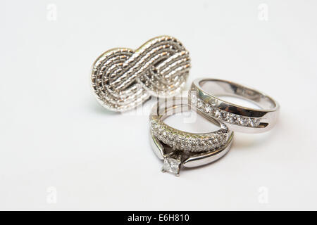 Or blanc et diamants Bandes de mariage une bague de fiançailles sont affichés en face d'un symbole de l'infini d'argent. Banque D'Images