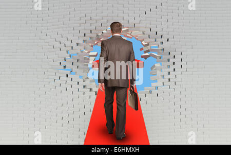 Businessman walking sur mur de brique percé flèche Banque D'Images