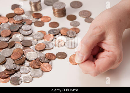 Woman's hand close up pincer un penny. Idée de la retraite et de ne pas avoir assez d'argent. Piles et des piles de pièces de monnaie prêt pour le comptage. Banque D'Images