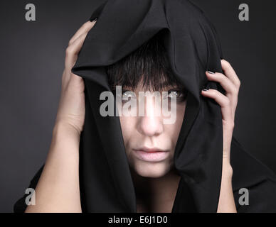 Effrayant femme avec un visage pâle. Recouvert de tissu noir. Banque D'Images