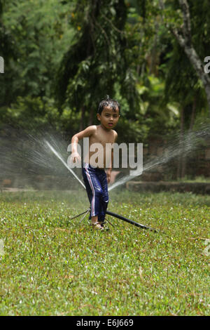 Petit garçon jouer dans le parc avec water sprinkler Banque D'Images