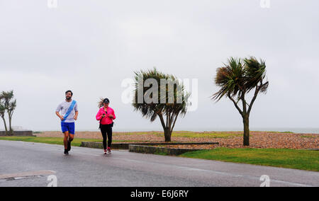 Worthing Sussex UK 25 Août 2014 - Un couple braver les éléments pour aller courir le long du front de mer dans l'affreux Worthing météo aujourd'humide et venteux a balayé le pays en cette maison de Banque Crédit Lundi : Simon Dack/Alamy Live News Banque D'Images