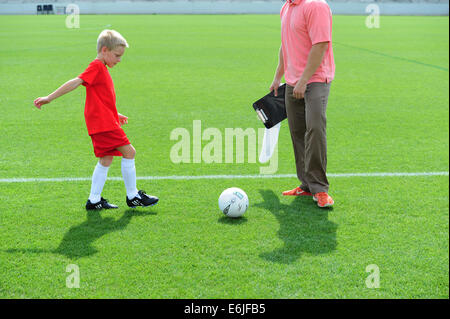 Boy 9 10 11 jouer au football futbol soccer sur terrain herbeux domaine réchauffe avec coach pratiquant Banque D'Images