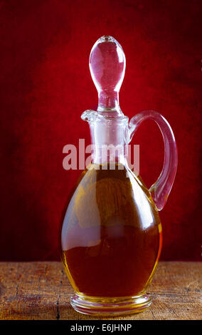 Carafe en verre avec de l'huile d'olive sur une vieille table en bois devant un mur rouge de style vintage Banque D'Images