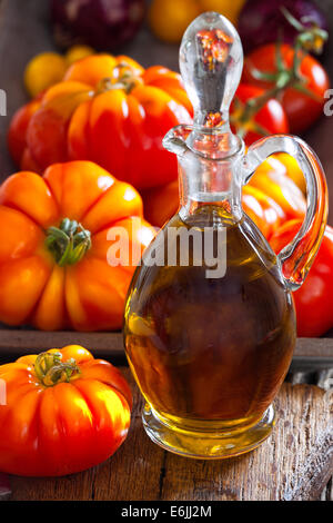 Carafe d'huile d'olive et tomates fraîches de bovins sur une vieille planche à découper rustique dans le style du pays Banque D'Images