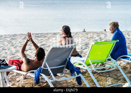 Trois personnes converser et profiter d'une plage tropicale tout en vous relaxant sur les chaises de plage. Banque D'Images