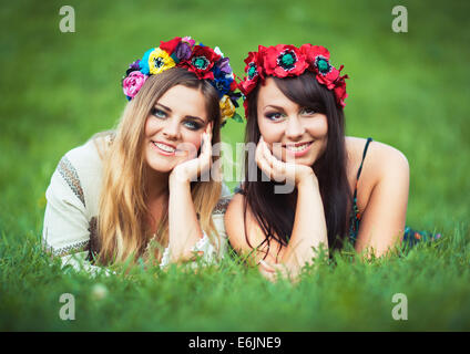 Deux beaux laughing girl in Ukrainian costumes nationaux se coucher sur l'herbe verte Banque D'Images