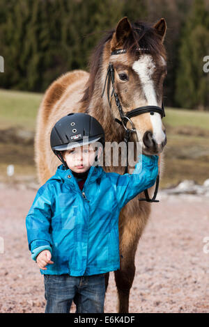 Jeune enfant portant un casque debout à côté d'un poney, dun, avec une patte, Tyrol, Autriche Banque D'Images