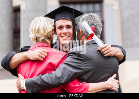 Beau jeune homme graduate serrant ses parents au moment de l'obtention du diplôme