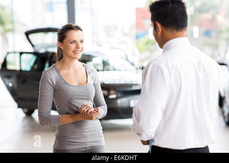 Vendeur de voiture sympathique parlant à une jeune femme à l'intérieur d'exposition Banque D'Images