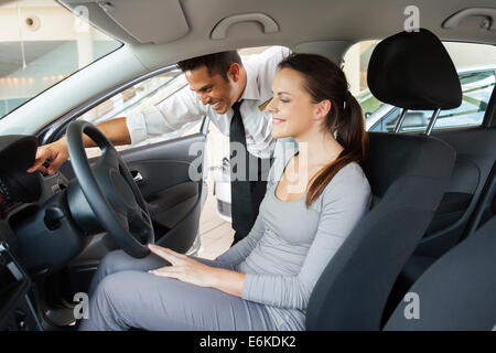 Les jeunes conseillers de vente voiture montrant une nouvelle voiture de client potentiel en showroom Banque D'Images