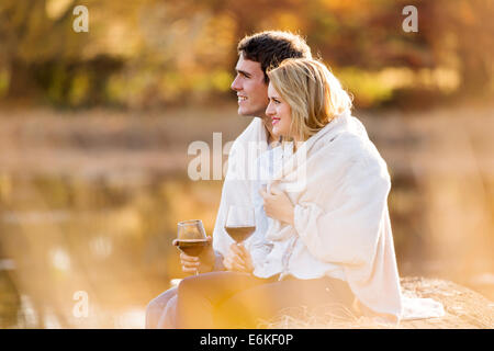 Couple ayant le vin rouge à l'extérieur par le lac d'automne Banque D'Images