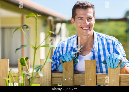 Bon à la young man standing by accueil jardin clôture avec pruner Banque D'Images