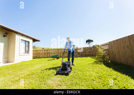 Cheerful young man mowing lawn à la maison Banque D'Images