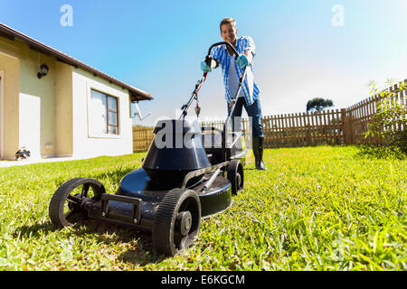 Low angle view of young man mowing lawn à la maison Banque D'Images