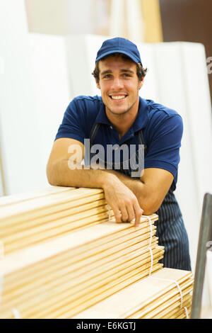 Heureux magasin worker standing next to stacked wood Banque D'Images