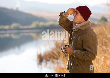 Happy young man holding coffee mug et à distance en en hiver matin Banque D'Images