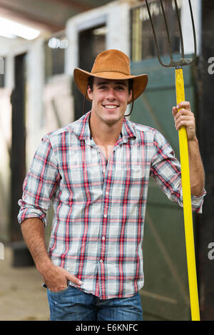 Beau cowboy tenant une fourche en stable Banque D'Images