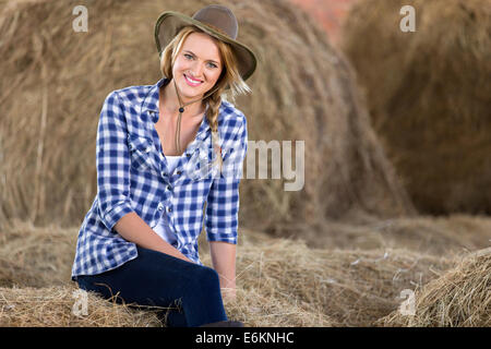 Belle cowgirl sitting on hay bales in barn Banque D'Images