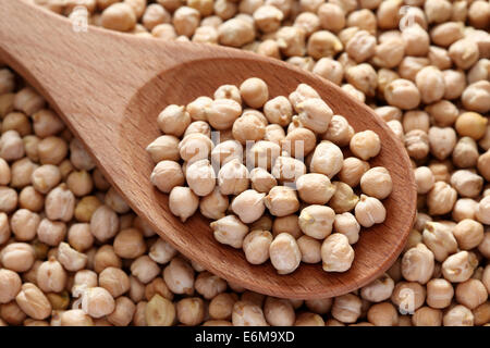 Les pois chiches dans une cuillère en bois sur fond de pois chiches. Banque D'Images