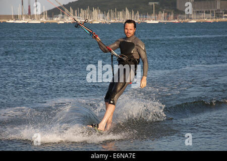 Sports d'eau. Male kiteboarder, porter une combinaison isothermique, excès de vitesse à travers l'eau du port de Portland, dans le Dorset, Angleterre, Royaume-Uni. Banque D'Images