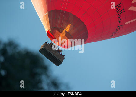 Virgin red hot air balloon flight passant basse avec un panier de passagers et d'allumer les brûleurs contre un ciel bleu profond. Banque D'Images