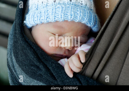 Un nouveau-né endormi dans un porte-bébé wrap Banque D'Images