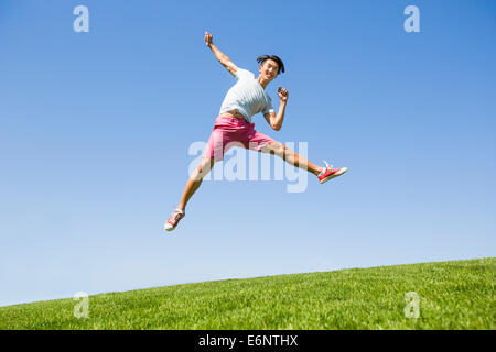 Cheerful young man jumping on grass Banque D'Images