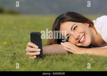 Pretty girl smiling en utilisant un téléphone intelligent couché dans l'herbe dans un parc ou d'une montagne Banque D'Images
