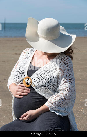 Des profils pregnant woman holding ses mains sur son ventre sur la plage avec du sable et de la mer