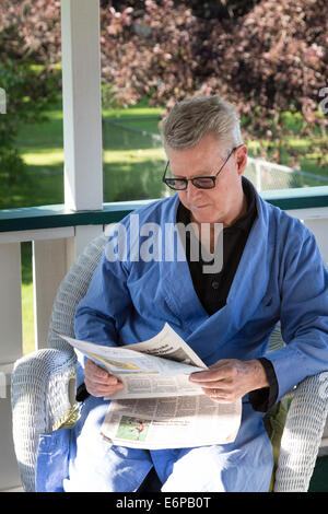 Homme mature sur terrasse arrière de sa maison lire les journaux du matin dans sa robe de chambre et pyjama, USA Banque D'Images