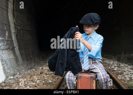 Vêtements vintage dans l'enfant est assis sur la route en face d'un tunnel. Banque D'Images