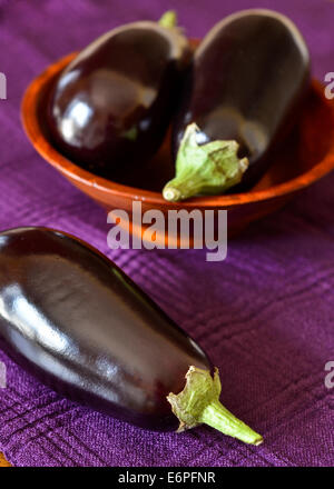 Poisson frais entier aubergines dans un bol en bois sur une serviette mauve Banque D'Images