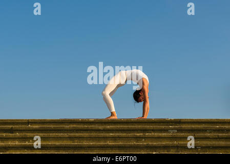 Jeune femme la pratique de l'Hatha Yoga, à l'extérieur, montrant la pose Chakrasana, Urdhva dhanurasana, poser des roues Banque D'Images