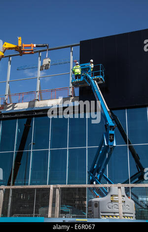 Dockland, front de mer de Liverpool, Merseyside, en cours de construction sur la façade du nouveau Centre d'exposition Kings Dock. Bardage extérieur étant apposée à l'aide de Clad Boy' élévateur vide périphérique connecté (filmés) de grue JCB 540 170 avec deux ouvriers, la fixation du bardage, en utilisant 'Easi-Lifts' godet d'extension. Liverpool dans le travail est le principal entrepreneur constructeur à l'appui pour le développement, la construction de l'EIG, avec accès à la main-d'œuvre locale et sous-traitant, ainsi qu'une aide en remplissant les offres d'emploi et d'apprentissage. Banque D'Images