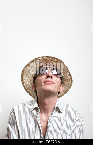 Jeune homme en chapeau de paille et lunettes de lever les yeux. Banque D'Images