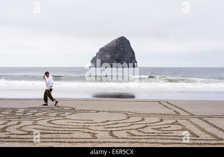 Chef d Kiawanda Rock autrement connu sous le nom de Haystack Rock à Pacific City Oregon avec un homme faisant un labyrinthe de plage au premier plan. Banque D'Images