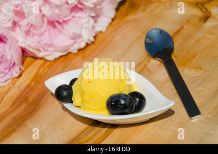 Une boule de sorbet au citron avec des bleuets dans un bol blanc avec une cuillère en argent et des fleurs roses Banque D'Images