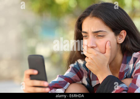 Adolescent inquiète girl looking at son smart phone dans un parc avec un arrière-plan flou Banque D'Images