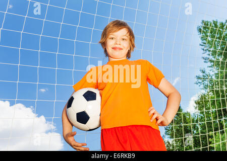 Garçon en tee-shirt orange avec football près de woodwork Banque D'Images