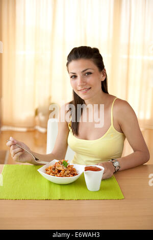 Young happy woman eating pâtes italiennes avec tomates, basilic et parmezan. Banque D'Images