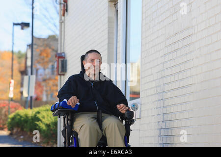 L'homme avec la moelle épinière et le bras de lésions nerveuses en fauteuil roulant motorisé à l'aide d'une rue publique Banque D'Images