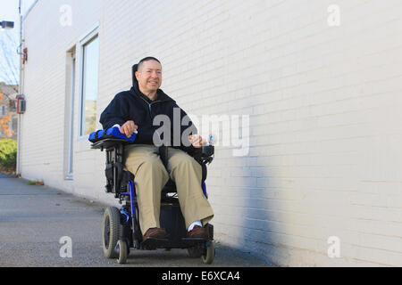 L'homme avec la moelle épinière et le bras de lésions nerveuses en fauteuil roulant motorisé à l'aide d'une rue publique Banque D'Images