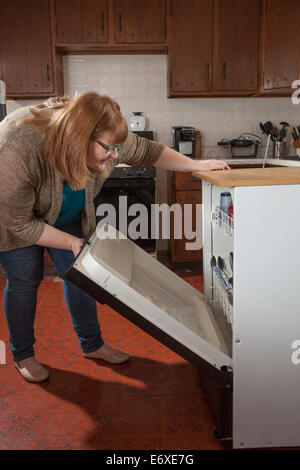 Femme qui est aveugle au sens de chargement du lave-vaisselle dans sa cuisine Banque D'Images