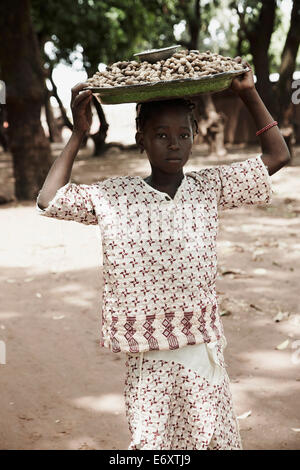 Girl exerçant la tête d'un plateau avec des cacahuètes pour marché, Yanfolila, région de Sikasso, Mali Banque D'Images