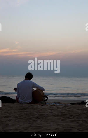 Tourist à jouer de la guitare sur la plage au coucher du soleil, d'Agonda, Goa, Inde Banque D'Images