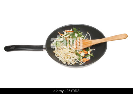 Faire sauter les légumes et les germes de soja dans un wok avec une spatule en bois isolés contre white Banque D'Images