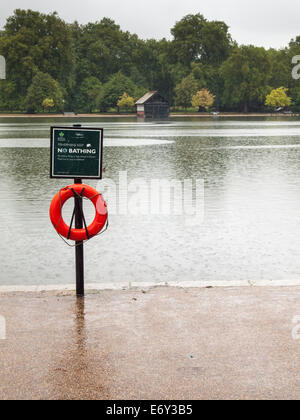 Le lac de plaisance de serpentine de Hyde Park dans de fortes pluies avec aucun signe de baignade et de la courroie de la vie en premier plan et remise en bateau derrière Banque D'Images